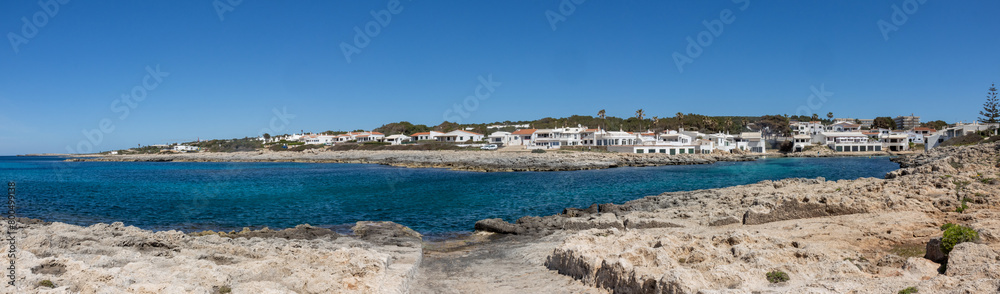 Panoramic photograph of the Biniancolla cove on the island of Menorca, offering a picturesque landscape of typical white houses, with an inlet on the coast. Spain
