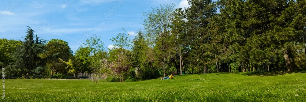 Tranquil city park in spring with lush green grass and trees, and a person relaxing on the slope, perfect for Earth Day and nature concepts Tranquil city park in spring with lush green grass and trees, and a person relaxing on the slope, perfect for Earth Day and nature concepts
