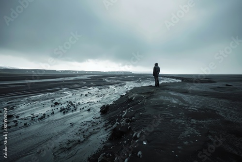 A lone figure stands on a desolate plain  looking out over a dark and stormy sea.
