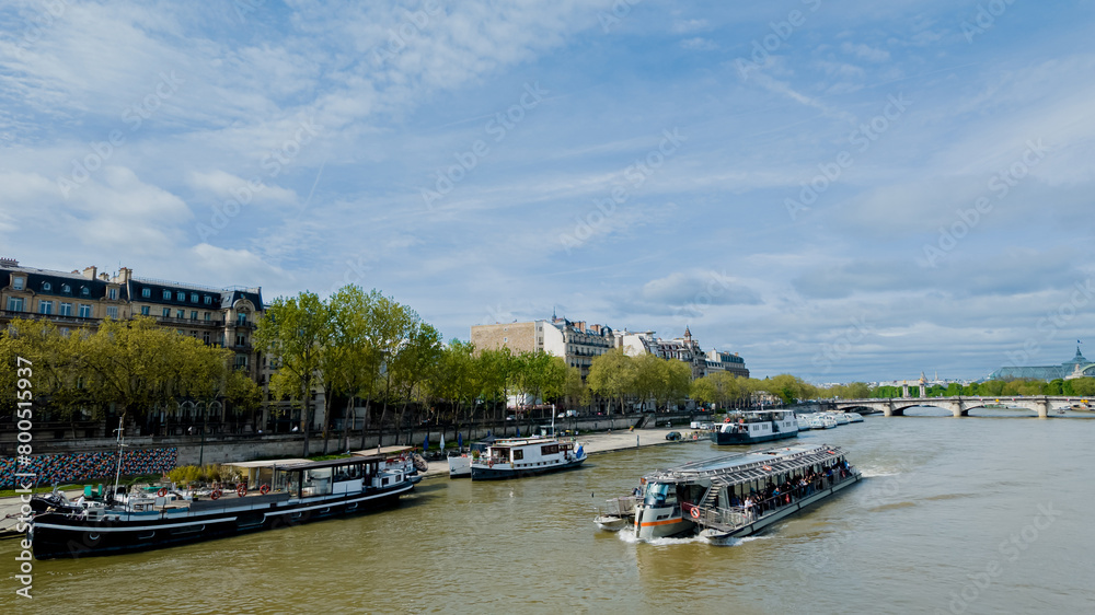 Naklejka premium Scenic view of the Seine river with tour boats and Parisian architecture, ideal for travel, tourism, and French culture themes