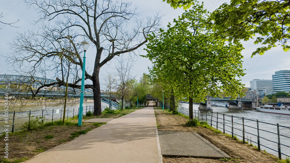 Tranquil riverside walkway with budding trees in early spring, ideal for urban tranquility themes and outdoor exercise in city settings