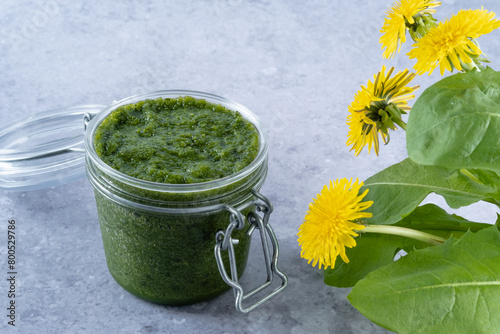 Dandelion greens pesto in jar on a gray background, side view. Appetizer, condiment or topping. Healthy vegan food.