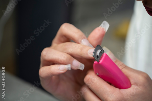 mains d'une femme réalisant sa manucure avec des capsules sur ses ongles à couper à la bonne longueur