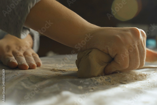 Women's hands knead dense clay for working on a potter's wheel.