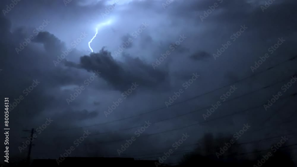 Low angle tracking shot of electricity pylon against stormy sky with lightning at night