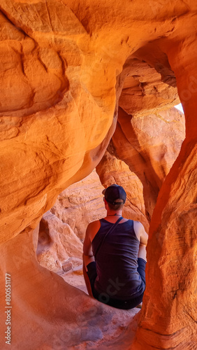 Man sitting in the fire cave and Windstone Arch in Valley of Fire State Park, Nevada, USA. Long, narrow slot canyon with sheer rock walls. Tranquil desert landscape of eroded sandstone formation photo