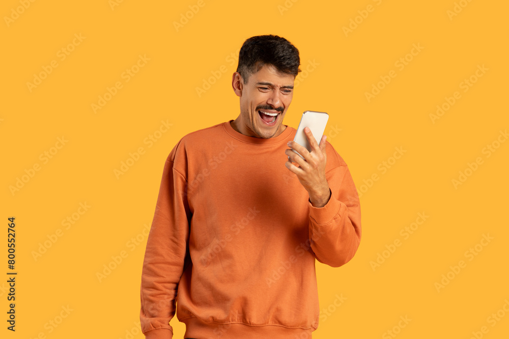 Man in Orange Sweater Holding Cell Phone And Exclaiming Man in Orange Sweater Holding Cell Phone And Exclaiming