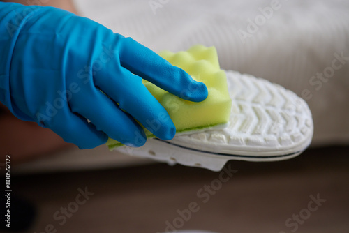 Applying cleaning foam from the bottle to white leather women's sneakers. Care for leather shoes, surface whitening.