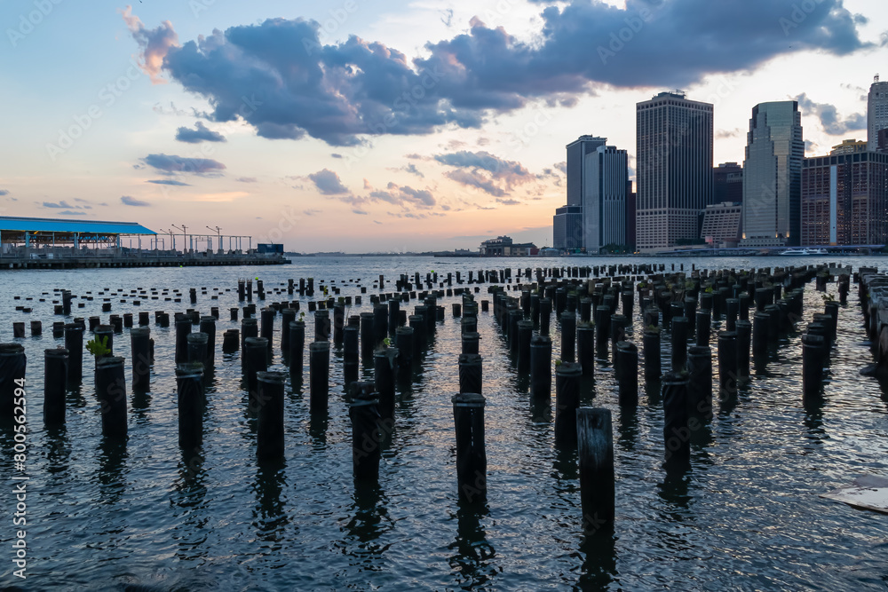 A pier on Hudson River in Brooklyn with the view on financial quarter of New York City. The sky is painted with soft colors of sunset. High skyscrapers reflecting on the water. Modern city.