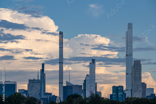 Captivating New York urban skyline at dusk with striking and modern skyscrapers reflecting on water seen from Jacqueline Kennedy Oasis Reservoir. The buildings are taller than surrounding clouds. photo