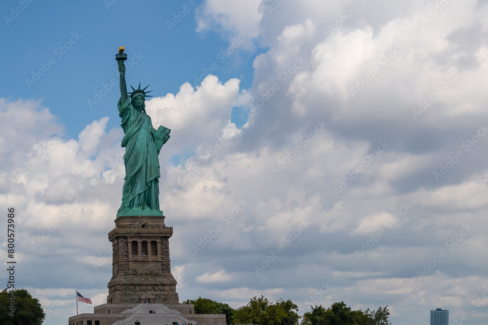 Obraz premium Iconic representation of freedom and independence, the Statue of Liberty with flaming torch on Liberty Island. The Lady on a Pedestal is surrounded by clouds. City landmark. American history.