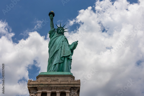A close up on an iconic representation of freedom and independence, the Statue of Liberty with flaming torch on Liberty Island. The Lady on a Pedestal is surrounded by clouds. American history. © Chris