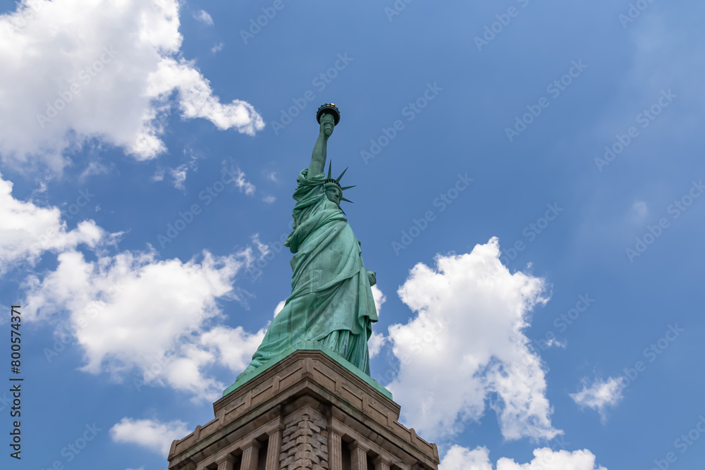 Fototapeta premium A close up on an iconic representation of freedom and independence, the Statue of Liberty with flaming torch on Liberty Island. The Lady on a Pedestal is surrounded by clouds. American history.