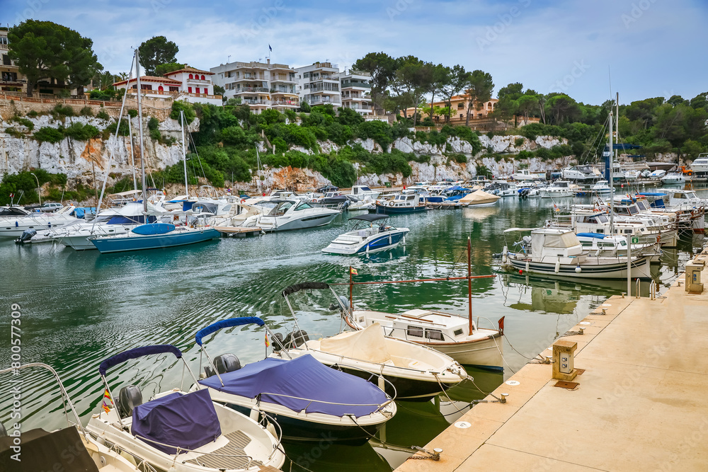 Amidst the tranquility of Porto Cristo harbor in Mallorca, moored boats adorn the waters, framed by the coastal beauty