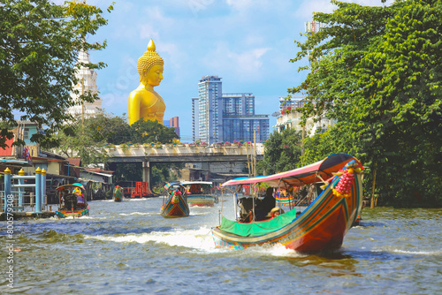 View of big  Buddha statue in Bangkok, Thailand (Wat Pak Nam Phasi Charoen) from canal with wooden houses and long tails boats
