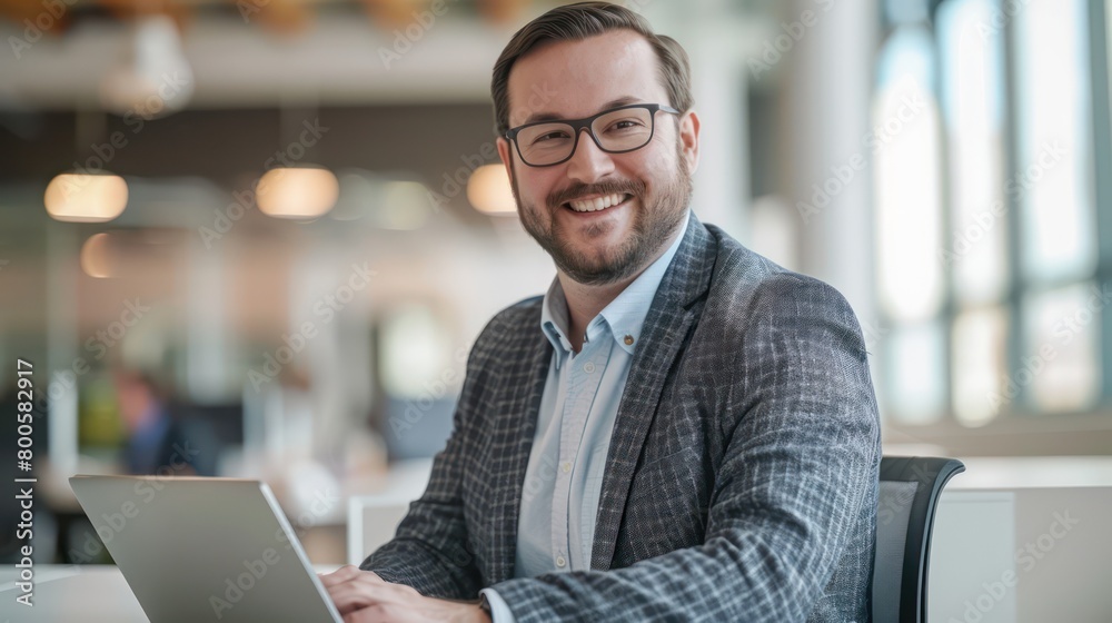 Young professional male in eyeglasses using a laptop and smiling in a modern office setup