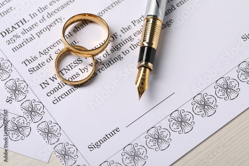 Marriage contract, gold rings and pen on light wooden table, top view