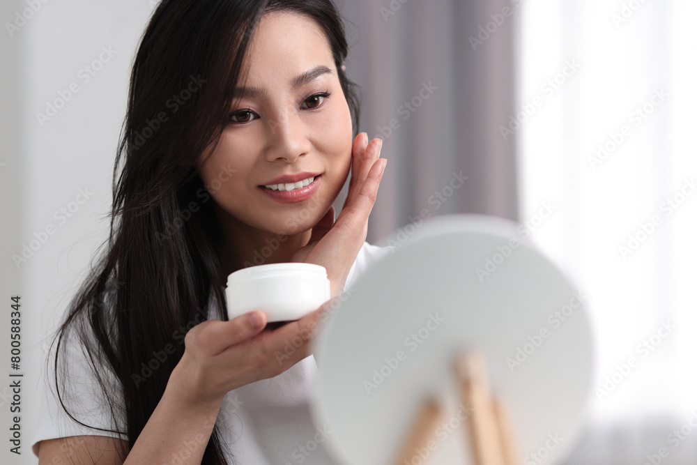 Happy woman applying face cream at home, space for text Happy woman applying face cream at home, space for text