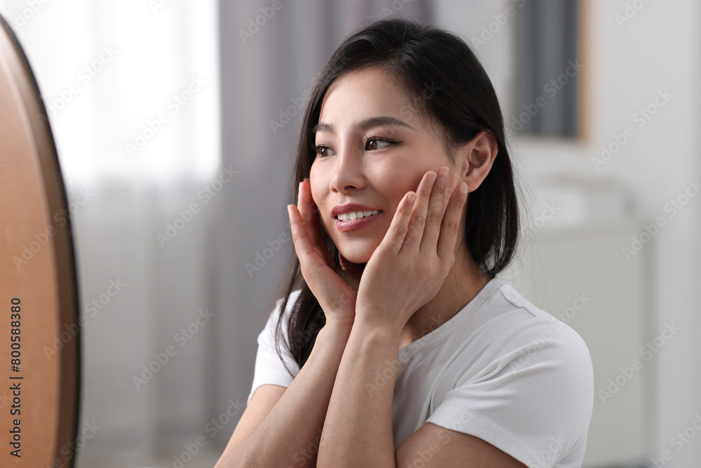 Woman with perfect skin looking at mirror indoors Woman with perfect skin looking at mirror indoors