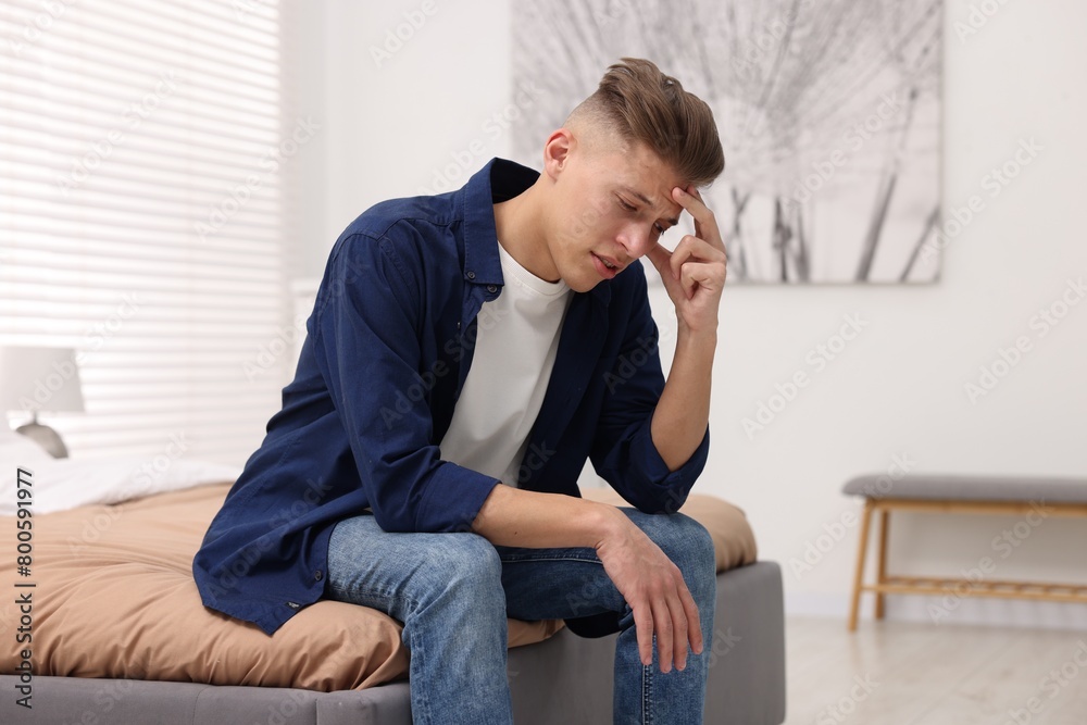 Overwhelmed man sitting on bed at home