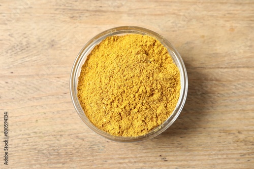 Curry powder in bowl on wooden table, top view