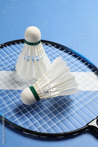 Feather badminton shuttlecocks and racket on blue background, closeup photo