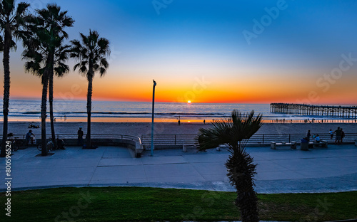 A sunset view of the Ocean and Pier at Pacific Beach in San Diego, California, with the setting sun casting a warm glow across the horizon. photo