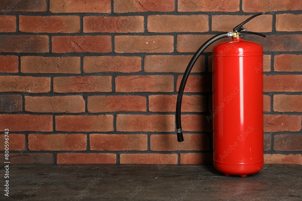 One red fire extinguisher near brick wall, space for text One red fire extinguisher near brick wall, space for text