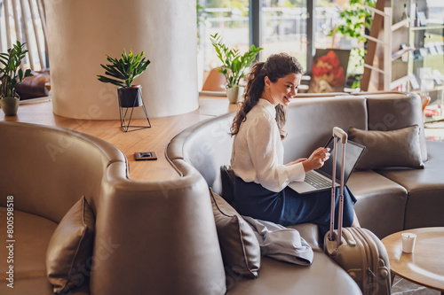 Businesswoman sitting in a hotel lobby, using laptop. Woman working on a business trip using online connections. Business lady went to business trip and stayed at the hotel.