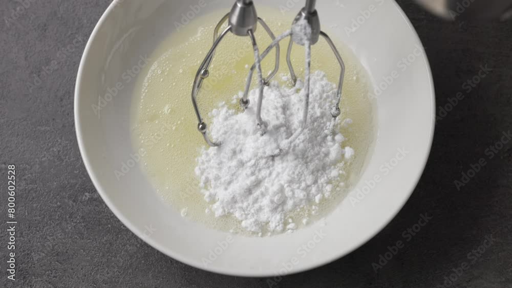 Cook adds powdered sugar to raw egg whites in a bowl, top view. Close-up of food Cook adds powdered sugar to raw egg whites in a bowl, top view. Close-up of food