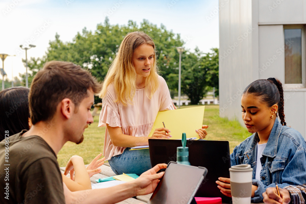 multiracial group of young students studying together or preparing a college project sitting on a bench on the university campus multiracial group of young students studying together or preparing a college project sitting on a bench on the university campus