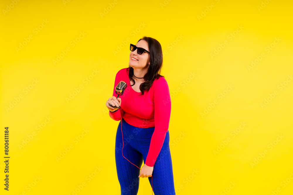 Woman in sport clothes sings into a wired microphone and claps her hands on a yellow background Woman in sport clothes sings into a wired microphone and claps her hands on a yellow background
