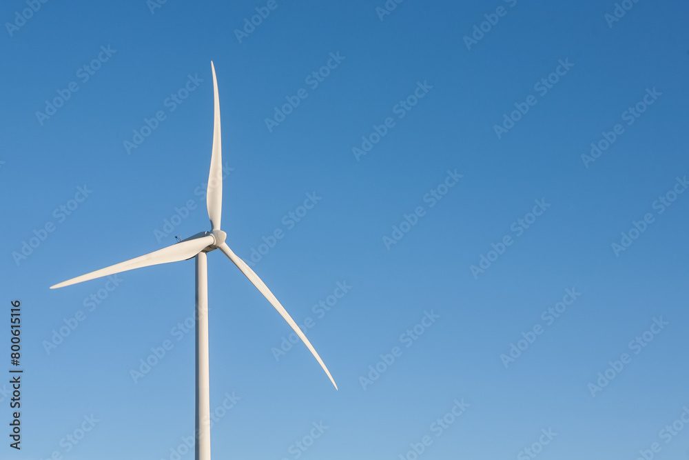 A wind turbine is standing tall in the sky, with a clear blue sky behind it A wind turbine is standing tall in the sky, with a clear blue sky behind it
