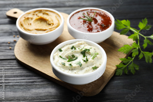 Different tasty sauces in bowls and parsley on black wooden table, closeup