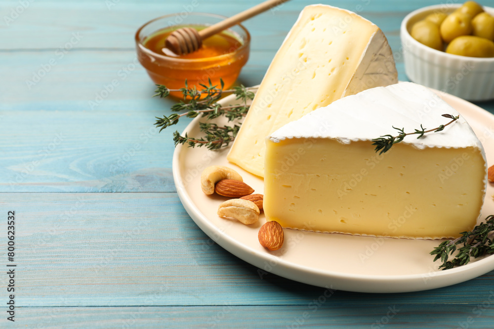 Tasty Camembert cheese with thyme and nuts on light blue wooden table, space for text
