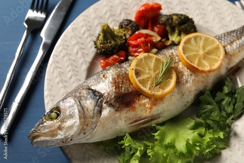 Delicious baked fish and vegetables served on blue wooden table, closeup