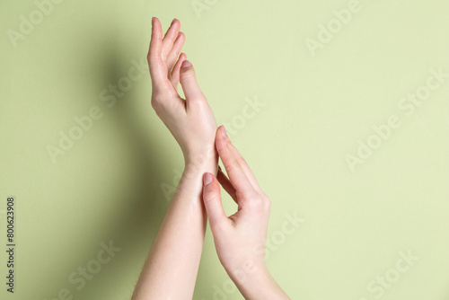 Woman applying cream on her hand against green background, closeup