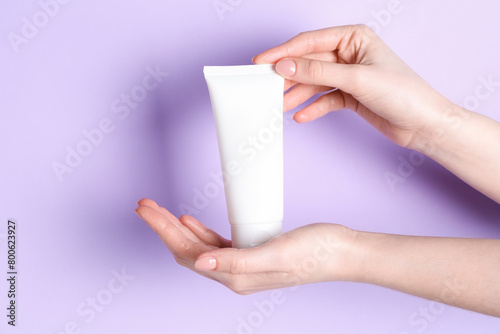 Woman holding tube of cream on violet background, closeup