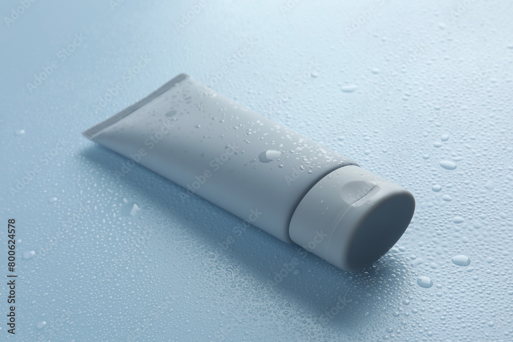 Moisturizing cream in tube on light blue background with water drops, closeup Moisturizing cream in tube on light blue background with water drops, closeup