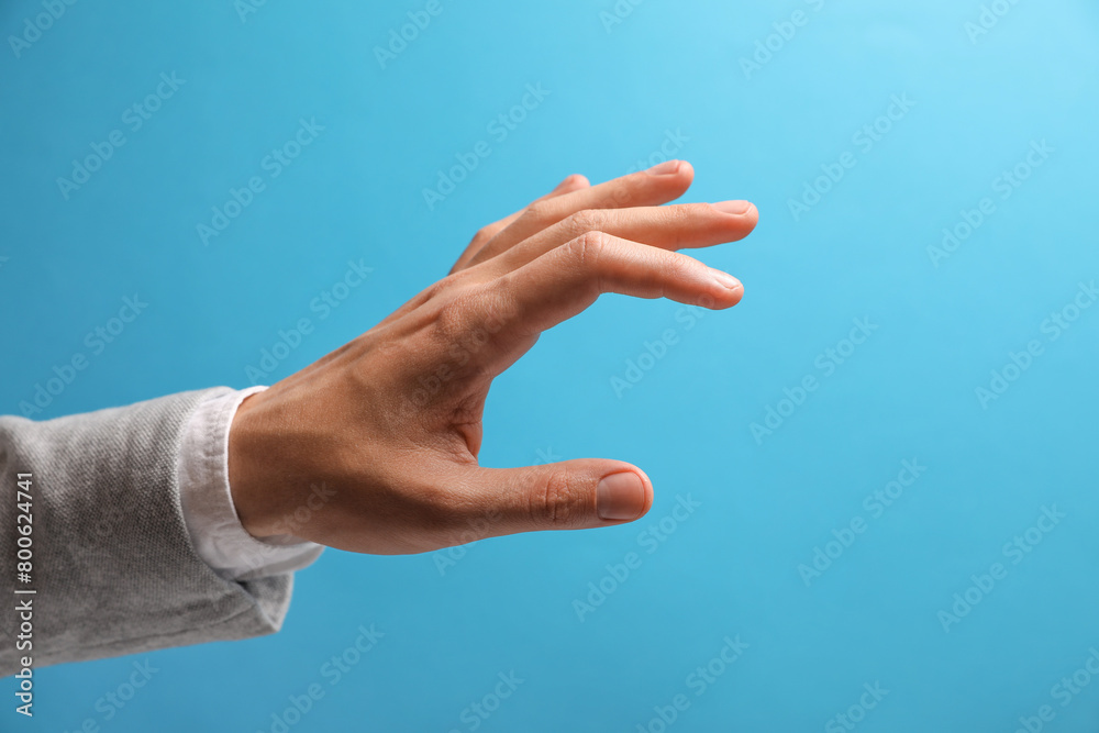 Man holding something in hand on light blue background, closeup. Space for text