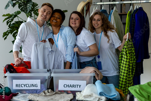 Group of volunteers, young women and man, sorting clothes in charitable foundation for charity donation, recycling. Concept of textile pollution, conscious consumption. Ecology, sustainable lifestyle photo