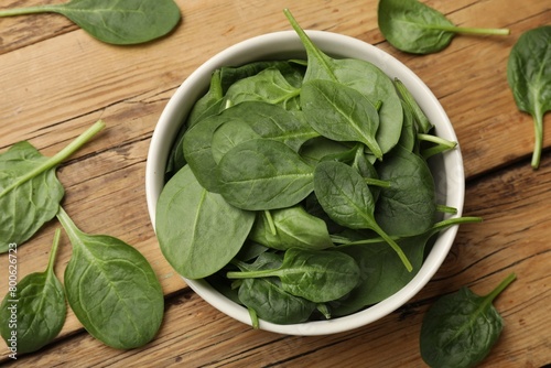 Fresh spinach leaves in bowl on wooden table, flat lay