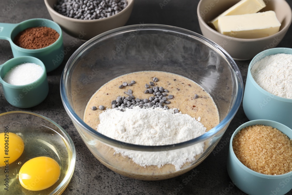 Raw dough with chocolate chips in bowl and ingredients on grey table, closeup