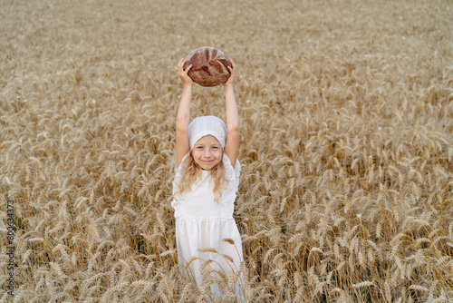 Little beautiful blonde girl with rye bread in a field of ears of rye © Надежда Урюпина