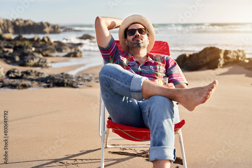 portrait mature man sitting relaxed drinking beer on the beach, enjoying solitude and sunset, escape concept	