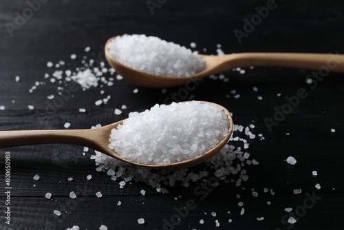 Organic salt in spoons on black wooden table, closeup