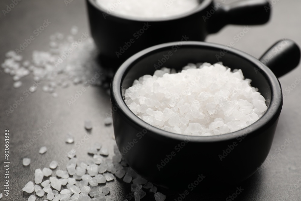 Natural salt in bowls on dark grey table, closeup