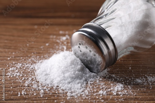 Overturned shaker with salt on wooden table, closeup