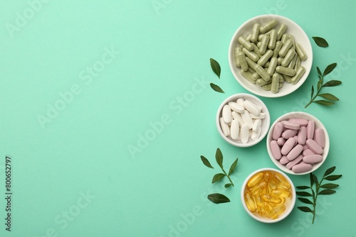 Different vitamin capsules in bowls and leaves on turquoise background, flat lay. Space for text