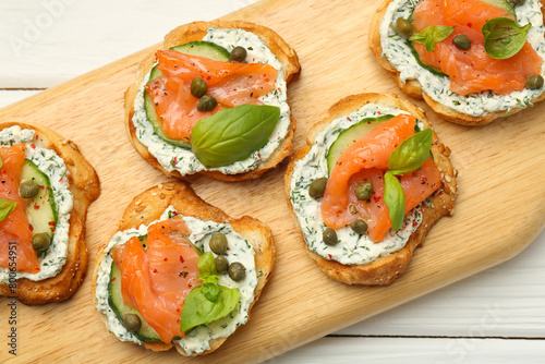 Tasty canapes with salmon, capers, cucumber and sauce on white wooden table, top view